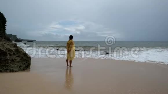 印度尼西亚巴厘岛一位穿着黄色雨衣的年轻女子在海滩上暴雨视频的预览图