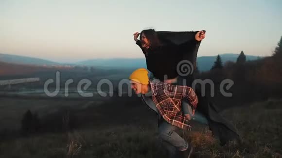 年轻的一对相爱的夫妇在享受高山的假期有魅力的男人把女朋友扛在肩上旋转着视频的预览图