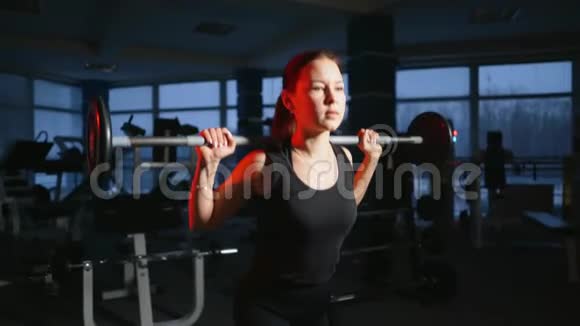 年轻漂亮的女孩在健身房里用杠铃在蹲上做运动改善臀部和臀部的肌肉视频的预览图