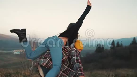 年轻的一对相爱的夫妇在享受高山的假期有魅力的男人把女朋友扛在肩上旋转着视频的预览图