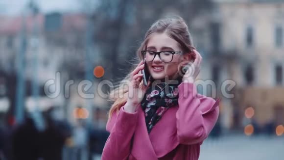 可爱的女孩打电话给某人然后愉快地交谈和微笑高兴时尚的外观粉红色的舒适外套视频的预览图