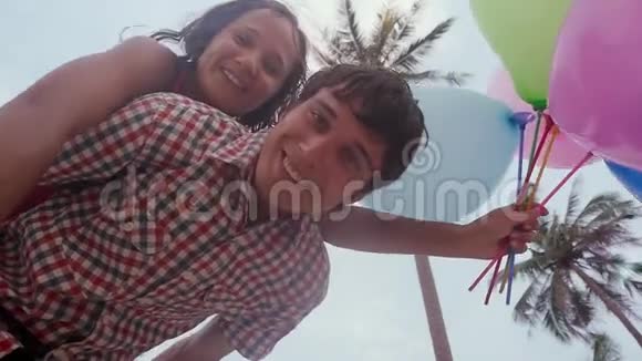男人肩膀上的幸福女孩的底部景色在背景上的棕榈树上拿着气球玩得很开心A视频的预览图