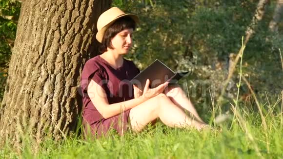 一个女孩正坐在户外的一棵树旁看书视频的预览图