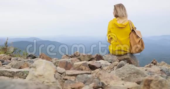 穿着黄色雨衣的女孩坐在山顶上欣赏着美丽的景色视频的预览图