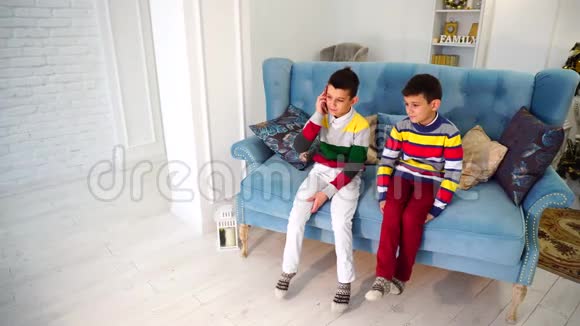 两个男孩弟弟轮流和奶奶在手机上交谈白天坐在明亮的房间里的蓝色沙发上视频的预览图