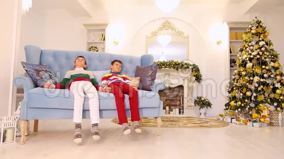 孩子们在节日装饰的房间里坐在蓝色的沙发上圣诞树和视频的预览图