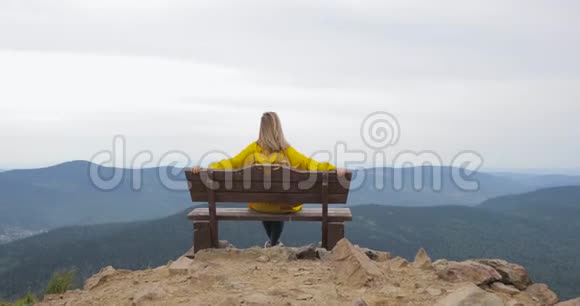 穿着黄色雨衣的女孩坐在山顶上欣赏着美丽的景色视频的预览图
