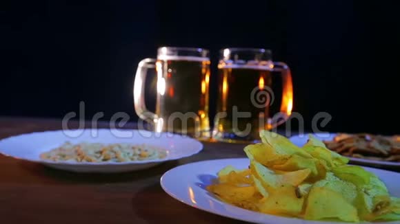 啤酒杯与泡沫啤酒在黑色背景上的木制桌子与小吃视频的预览图