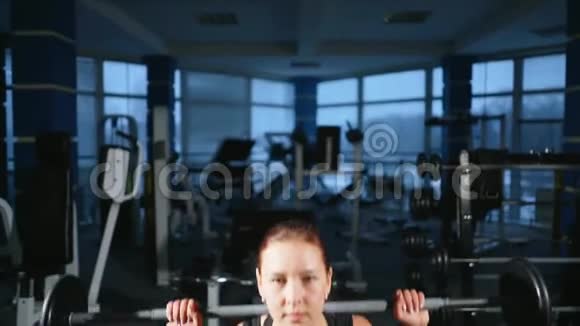 年轻漂亮的女孩在健身房里用杠铃在蹲上做运动改善臀部和臀部的肌肉视频的预览图