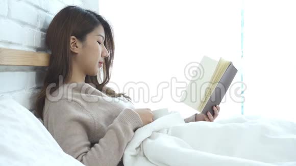 美丽的亚洲女人在卧室的床上享受着温咖啡和读书视频的预览图