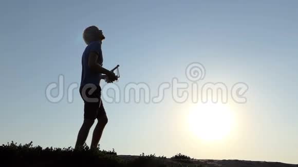 在日落时分年轻人用他的面板操纵着一架飞行无人机视频的预览图