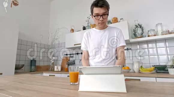 家中有魅力的男人在厨房里用平板电脑发送信息社交媒体微笑着享受现代生活方式视频的预览图