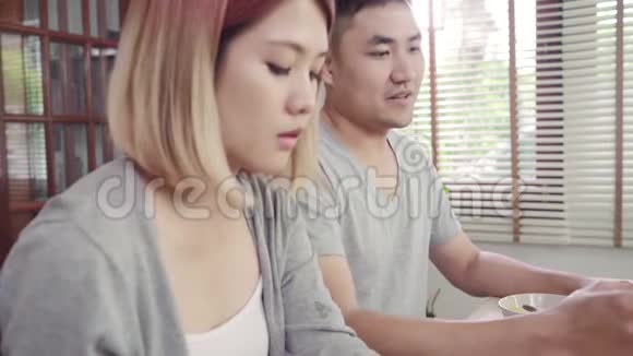 漂亮的亚洲年轻夫妇在吃早餐时一边拿着报纸和手机一边在桌子上分心视频的预览图