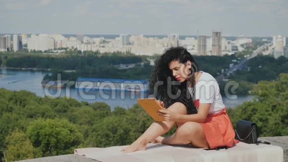 美丽的女孩用平板电脑放松城市背景视频的预览图