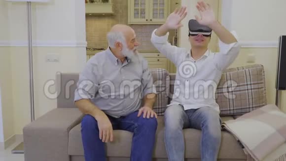 年轻人在家里和祖父一起测试虚拟现实眼镜视频的预览图