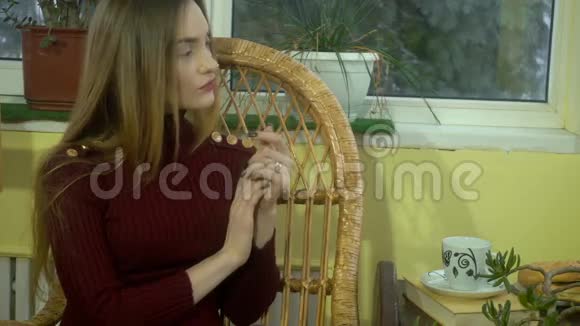 可爱的年轻女孩美丽的化妆坐在柳条椅子上喝热咖啡看着窗外下雪视频的预览图