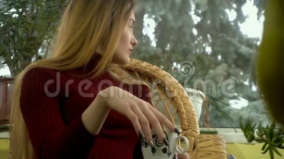 年轻女子坐在一把柳条椅子上望着窗外身后降着雪享受着一杯视频的预览图