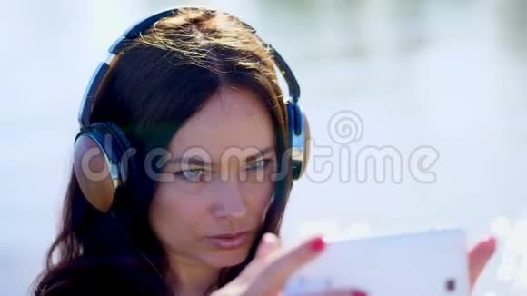夏天户外一个美丽的女人的肖像留着长长的黑发听着手机耳机里的音乐视频的预览图