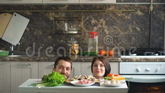 在厨房做饭的时候一对美丽的微笑的夫妇在餐桌上玩着亲吻着蔬菜视频的预览图