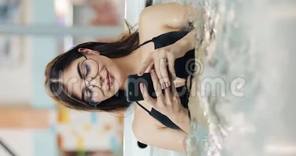 垂直视频美丽的年轻女子使用智能手机放松按摩浴缸带手机的女孩在游泳池里放松视频的预览图
