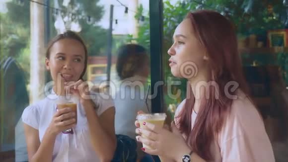 两个女孩在一家户外咖啡馆聊天他们在街上喝鸡尾酒4K慢镜头拍摄视频的预览图
