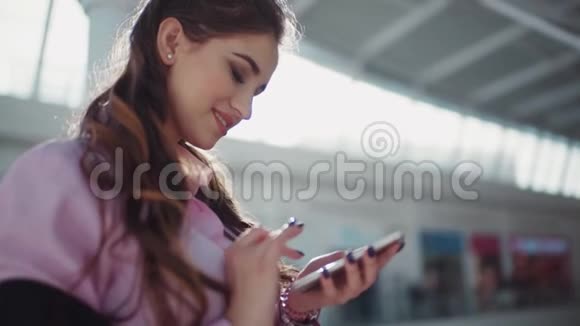 穿着粉红色衬衫的漂亮化妆的漂亮微笑的女人在购物中心那个女孩专心于她视频的预览图