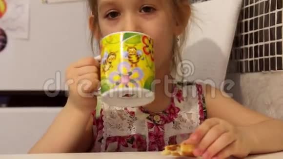 可爱的小女孩正在吃早餐孩子吃饼干喝茶视频的预览图