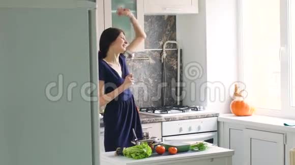 有趣的女人在家厨房做饭时用大勺子跳舞唱歌视频的预览图
