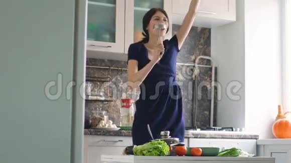 有趣的女人在家厨房做饭时用大勺子跳舞唱歌视频的预览图