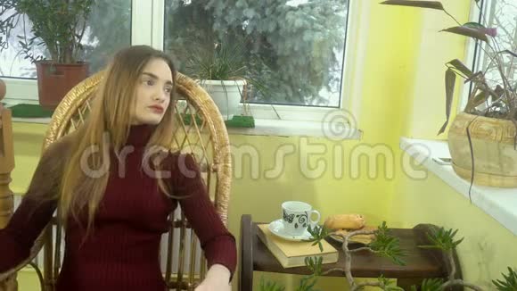 美丽的年轻女子化妆漂亮坐在柳条摇椅上望着窗外身后是雪视频的预览图