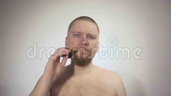 男人梳理他的红色胡须白色背景上的木制梳子视频的预览图