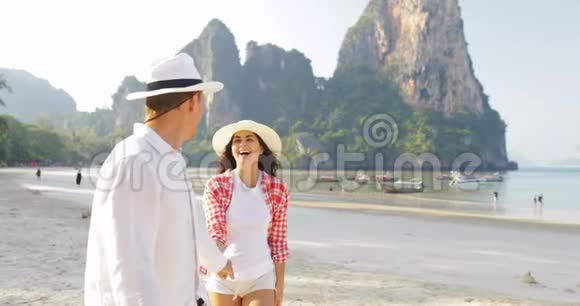 男主角情侣在沙滩上散步手牵手在度假中与年轻游客交谈视频的预览图