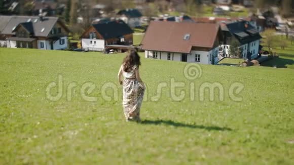 在群山背景的草地上穿着乡村长裙的女孩的后景旋转视频的预览图