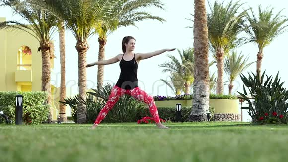 运动女孩做基础练习从瑜伽赤脚站在草坪上穿着时尚运动服装的布鲁内特视频的预览图
