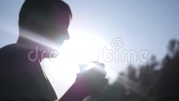 一个年轻健康的人从玻璃杯中喝干净的水站在轮廓光线和光线中的太阳旁边视频的预览图