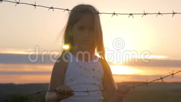 小女孩在铁丝网后面日落孩子手握着电线自由和移民的概念视频的预览图