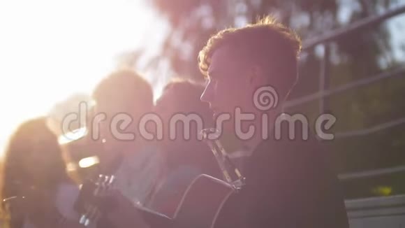日落时分年轻的朋友在公园里用吉他唱歌视频的预览图