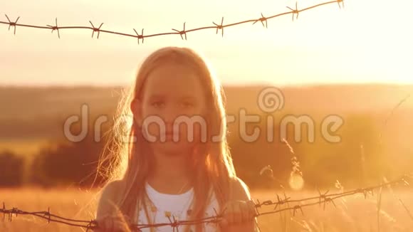 小女孩在铁丝网后面日落孩子手握着电线自由和移民的概念视频的预览图