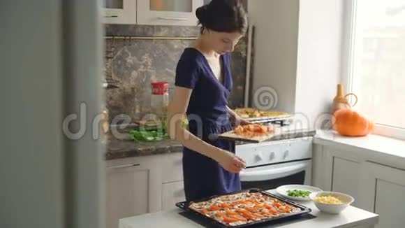 年轻漂亮的女厨师在家里的厨房里把番茄放在披萨面团上视频的预览图