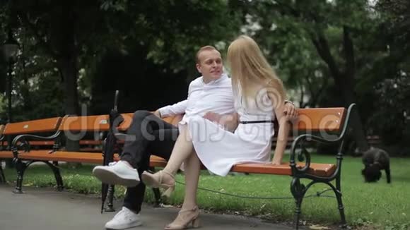 漂亮的夫妇坐在公园的长凳上金发男人和女人花时间去做他们带着黑伞视频的预览图