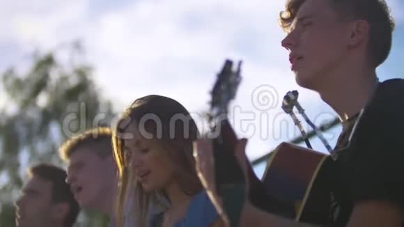 吸引人的年轻朋友嬉皮士在夏日日落时用吉他唱歌视频的预览图