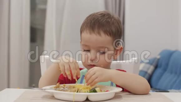 小孩子坐在围兜里的一张桌子旁吃自己的意大利面可爱的宝宝心甘情愿地吃可爱的小宝宝视频的预览图