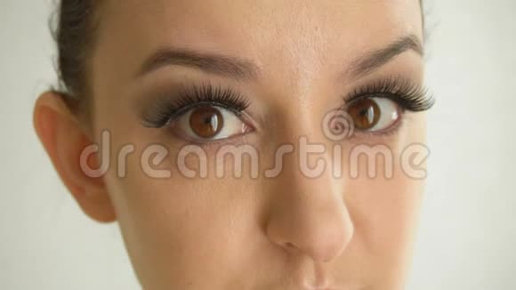 长着假睫毛和棕色眼睛的女性脸看着相机化妆时尚的特写美女模特视频的预览图