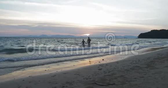 快乐的夫妻在沙滩上奔跑手牵手在夕阳下的青年男女在暑假视频的预览图