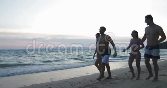 在日落时分在沙滩上散步的人群夏季度假期间的两对混合种族夫妇交流视频的预览图