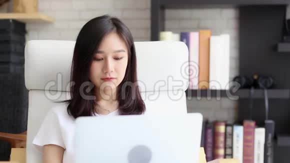 美丽的肖像自由职业亚洲女性微笑着坐在客厅的沙发上快乐地在网上笔记本电脑上工作视频的预览图