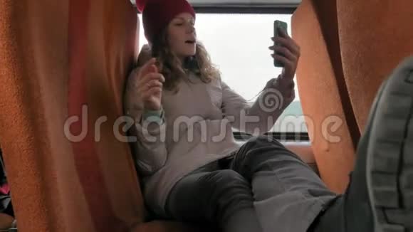 年轻开朗的女人戴着红帽子在一个悲伤的日子乘公共汽车旅行她听音乐视频的预览图