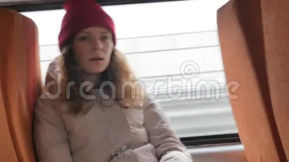 年轻开朗的女人戴着红帽子在一个悲伤的日子乘公共汽车旅行她听音乐视频的预览图