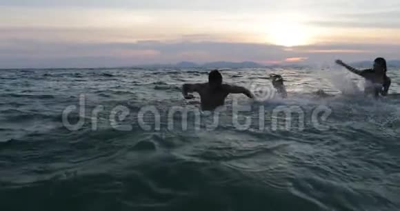 一群在日落时分在海中嬉戏的朋友一群快乐的年轻人在暑假一起在沙滩上游泳视频的预览图