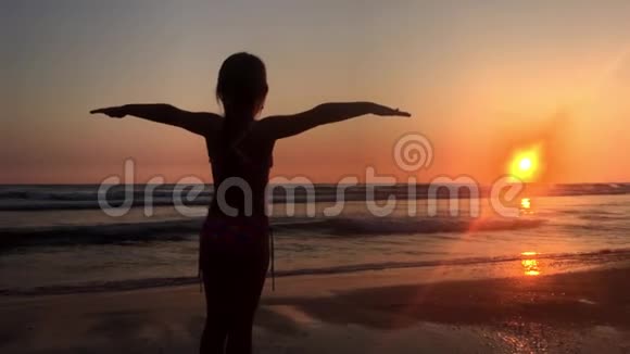 快乐的小女孩在海上张开双手享受自由夕阳海边海滩欢呼雀跃的女徒步旅行者张开双臂视频的预览图